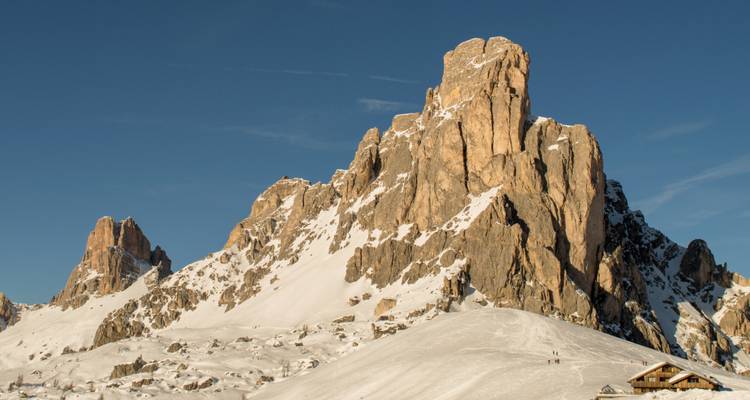 Sommets montagneux enneigés avec un ciel dégagé, petits bâtiments à la base.