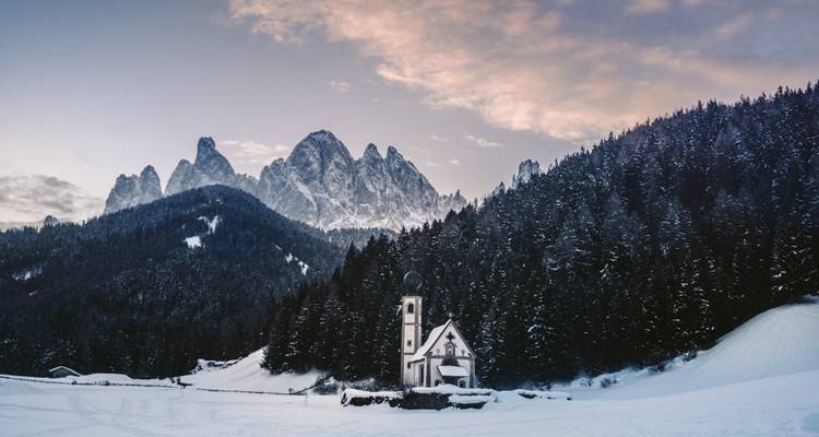 Paysage enneigé avec une petite église, entourée de forêt et de montagnes.