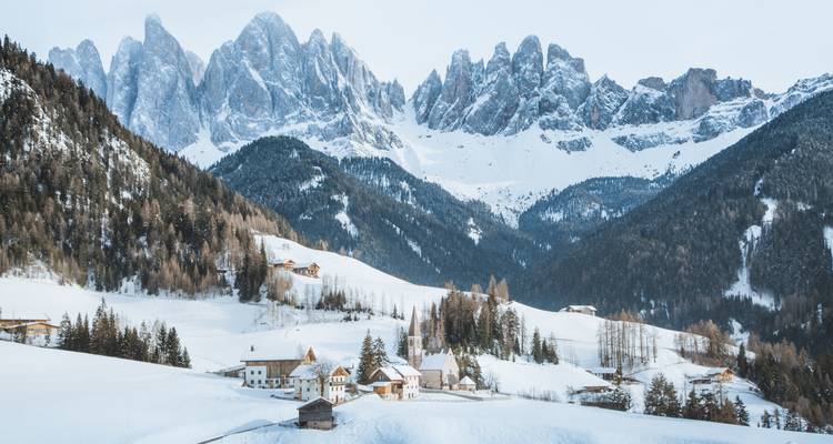 Village alpin enneigé avec des montagnes majestueuses en arrière-plan.