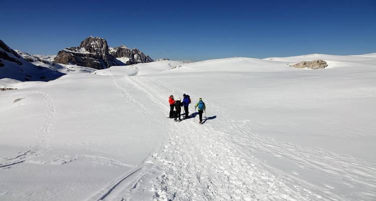 Groupe de personnes marchant sur un paysage enneigé avec des sommets de montagnes en arrière-plan.