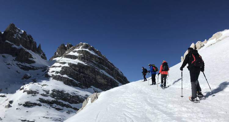 Des personnes faisant de la raquette sur une montagne avec des pics rocheux en arrière-plan.