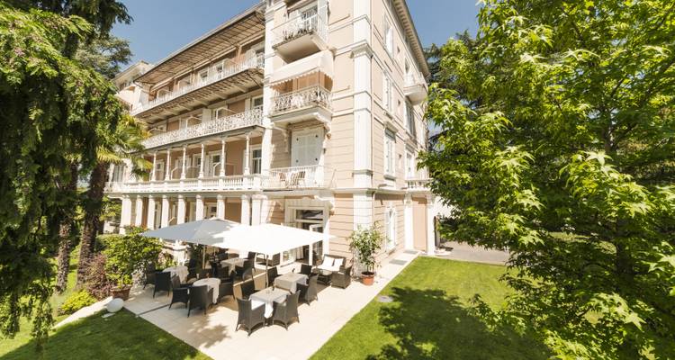 A grand hotel with outdoor seating area and lush greenery.