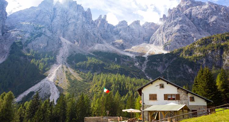 Refuge de montagne avec drapeau italien, entouré de forêt et de pics rocheux.