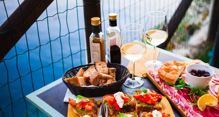 Table extérieure donnant sur la mer avec bruschettas, charcuterie et verres de vin blanc.