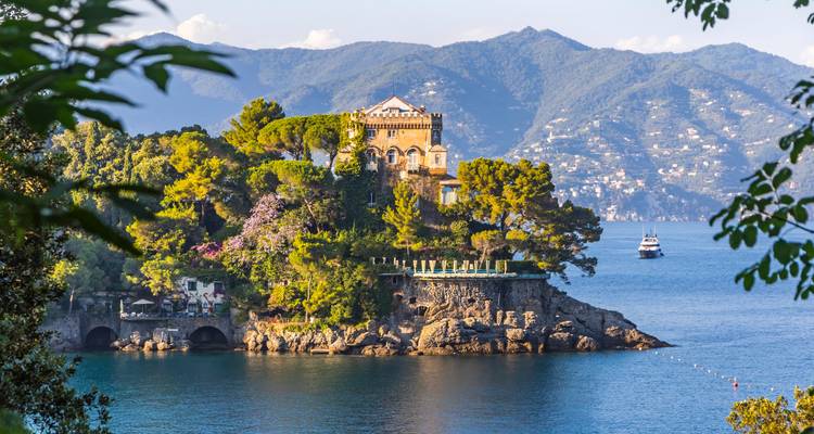 Villa élégante entourée de pins et de jardins sur une presqu'île rocheuse dans des eaux saphir avec des montagnes au-delà.