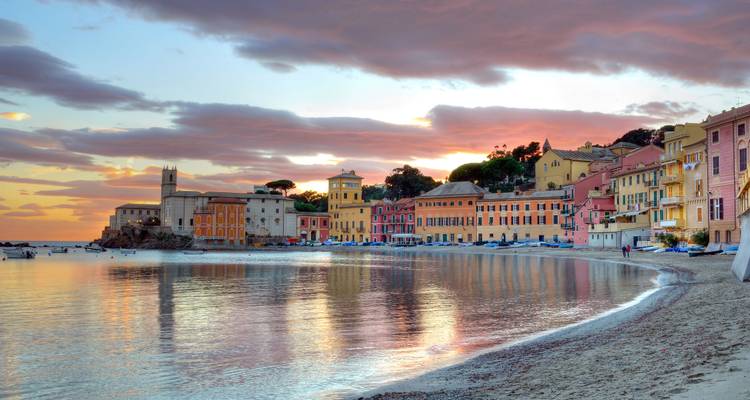 Les couleurs du coucher de soleil se reflètent sur les eaux calmes de la baie devant des bâtiments aux teintes pastel et un clocher d'église.