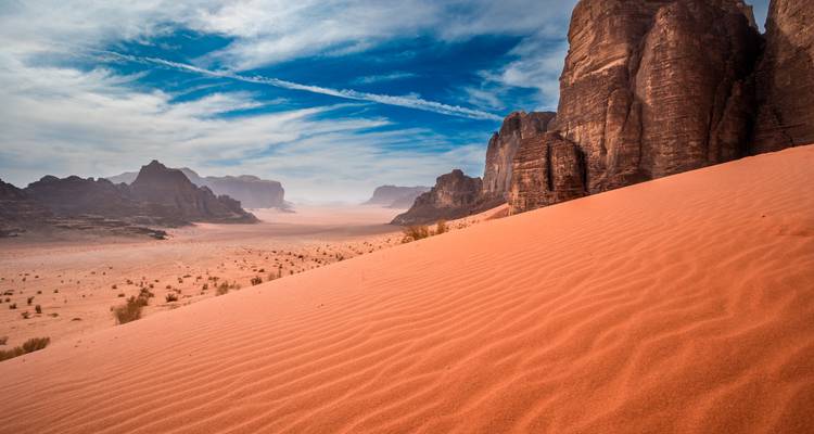 Desert landscape with orange sand dunes and rocky outcrops.