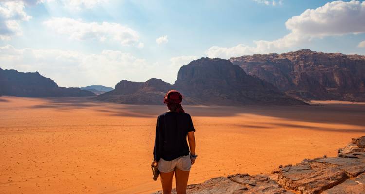 Person standing on a rocky outcrop looking at desert mountains.