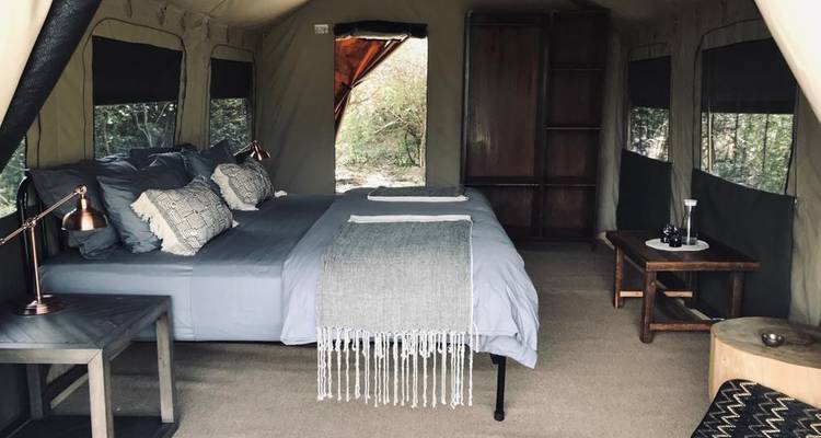 Innenraum eines stilvollen Canvas-Safarizeits mit ordentlich gemachtem Doppelbett, Beistelltischen und sanfter Beleuchtung, eingerichtet als komfortable Unterkunft in der Wildnis.