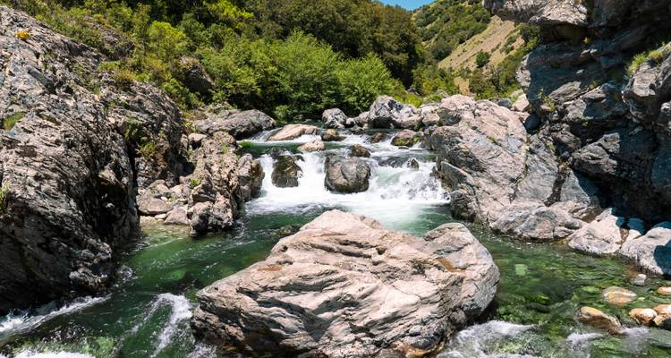 Een levendige bergbeek stroomt tussen rotsige rotsen door een weelderig mediterraan bos.