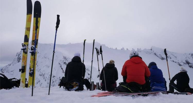 Groupe de skieurs assis dans la neige avec des bâtons de ski et des sommets enneigés en vue.