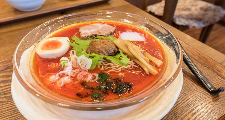 Schüssel mit Ramen mit Eiern, Fleisch und Gemüse auf einem Holztisch.
