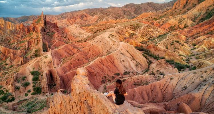 Person, die am Rand felsigen Geländes sitzt und dramatische Landschaften überblickt.