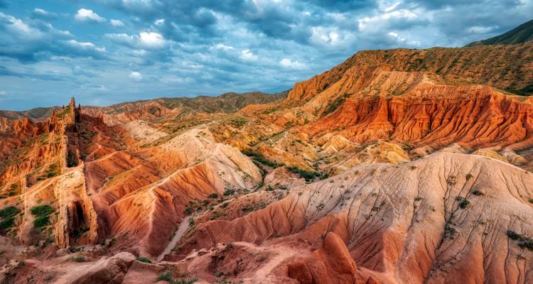 Bunte Gesteinsformationen in einer zerklüfteten Landschaft unter bewölktem Himmel.