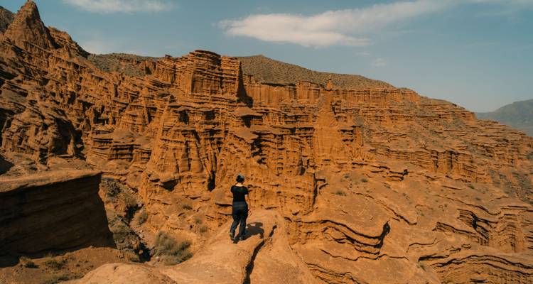 Een persoon die staat op een ruige rotsvormatie in een canyonlandschap.