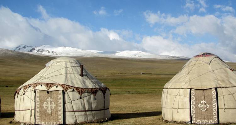 Traditionelle Jurten in einer weiten Naturlandschaft mit schneebedeckten Bergen.
