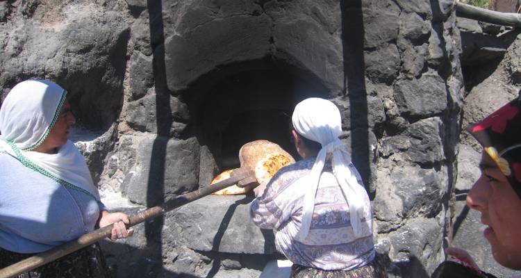 Two women baking bread in a stone oven.