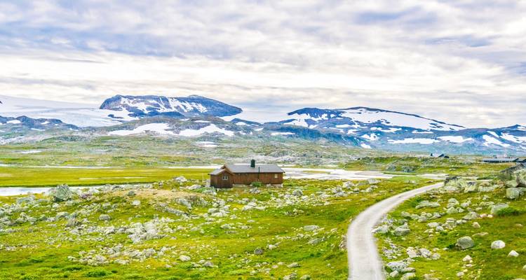 Scenic view of a house and path leading to snowy mountain peaks.