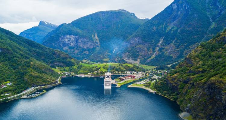 Aerial view of a fjord with a cruise ship surrounded by mountains.