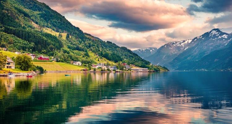 Quaint village by a fjord with snow-capped mountains in the background.