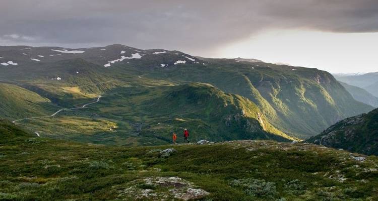 Hikers on a green mountainous terrain with clouds overhead.