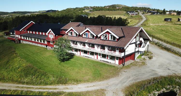Rotes Gebäude eingebettet in eine grüne Landschaft mit entfernten Häusern.