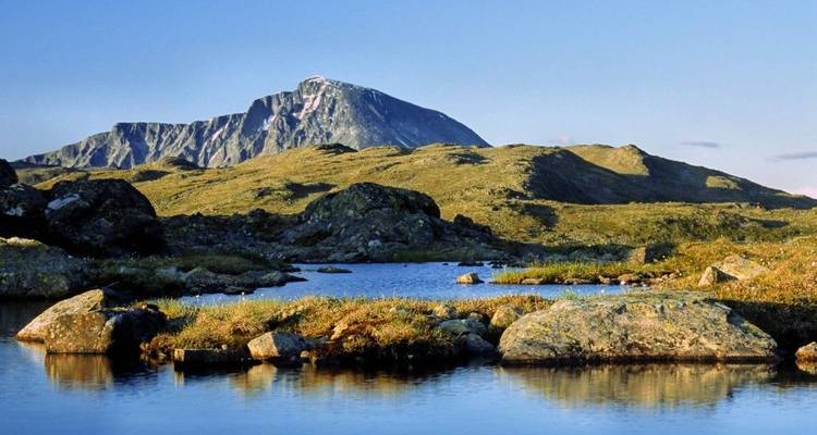 Mountain peak with grassy foreground and a calm stream.