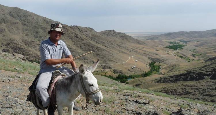 Mann auf einem Esel mit bergiger Landschaft im Hintergrund.