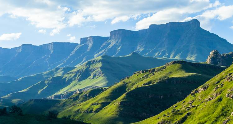 Mountain range with steep cliffs and green valleys, likely in Drakensberg.