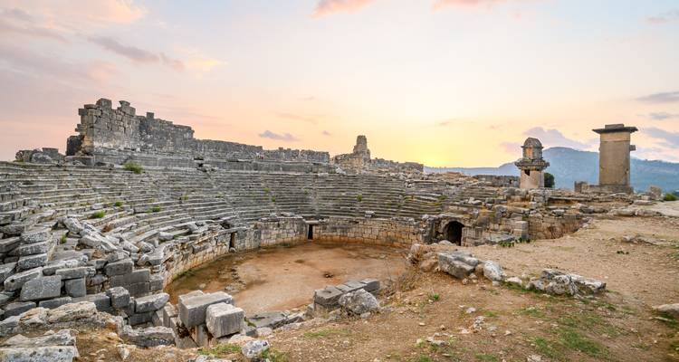 Ancient amphitheater ruins under a cloudy sunset sky.