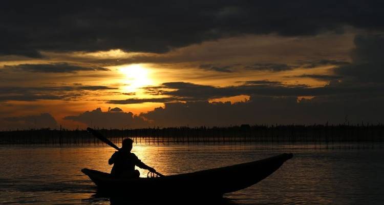 Een persoon die een boot roeiert bij zonsondergang met een silhouet van de boot en een dramatische lucht.