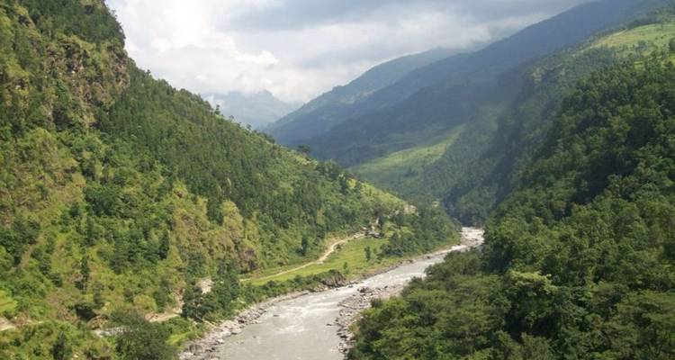 Een rivier die zich een weg baant door weelderige groene bergen onder een gedeeltelijk bewolkte hemel.