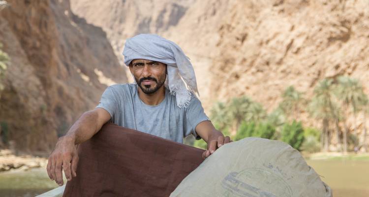 Man in traditional Middle Eastern attire in a rocky desert landscape.