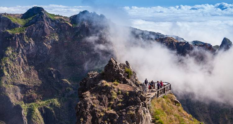 Excursionistas en una plataforma mirador rodeados de nubes a mitad de camino hacia los picos escarpados.