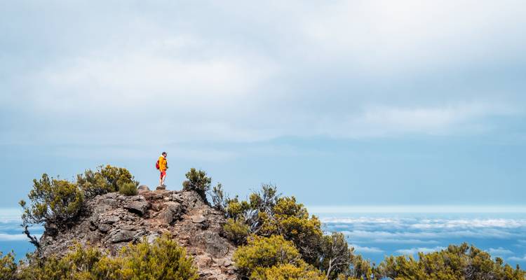 Excursionista solitario en chaqueta brillante de pie en la cima rocosa sobre un mar de nubes.