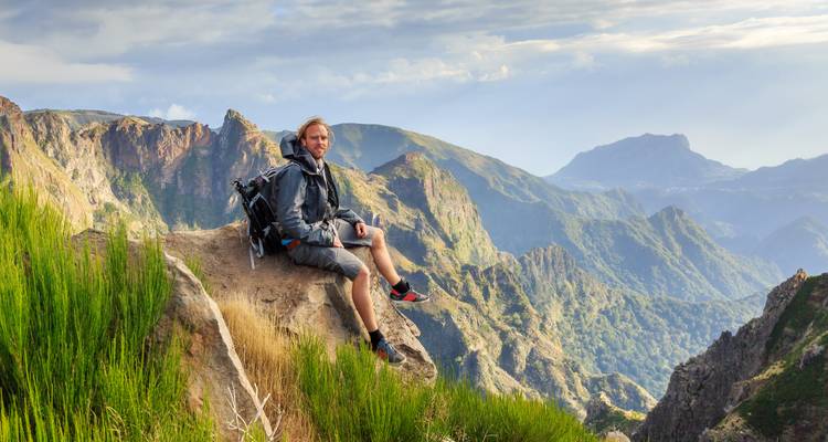 Mochilero descansando en una cornisa de acantilado con montañas verdes espectaculares por todos lados.