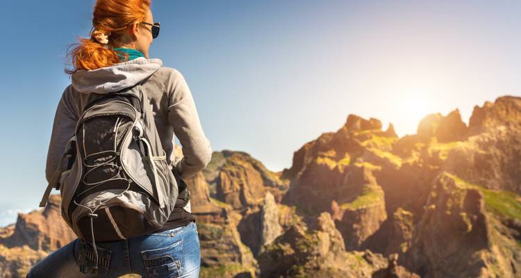Person with a backpack looking at rocky mountains in sunlight.