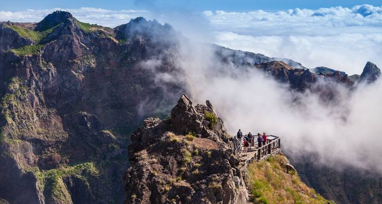 Visitantes en una plataforma de observación de madera rodeados de nubes arremolinadas en el dramático pico montañoso de Madeira.