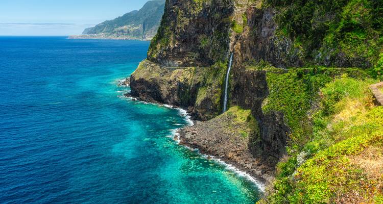 Paysage côtier avec des falaises et une cascade se jetant dans la mer.