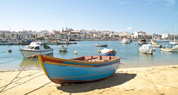 Barca de pesca de madera pintada en una playa de arena con un pueblo portuario de fondo bajo cielos azules