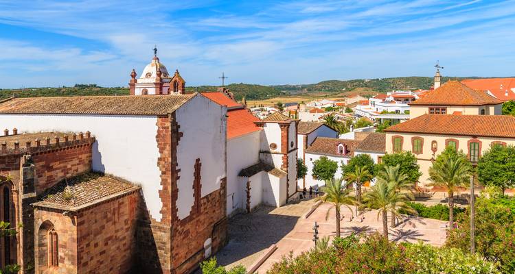 Iglesia histórica y techos de azulejos con vistas a una soleada plaza de pueblo portuguesa con palmeras
