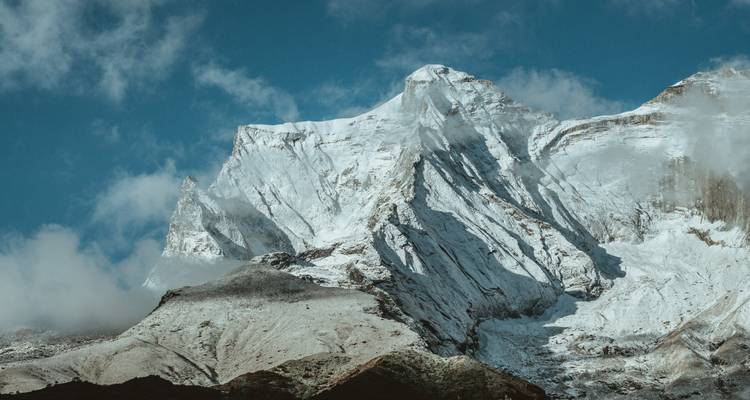 Indrukwekkende bergpiek met sneeuw en wolken tegen een heldere hemel.