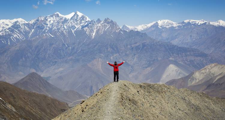 Een wandelaar met uitgestrekte armen die naar bergtoppen staart.