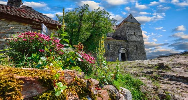 Une église en pierre entourée de fleurs éclatantes et de verdure.