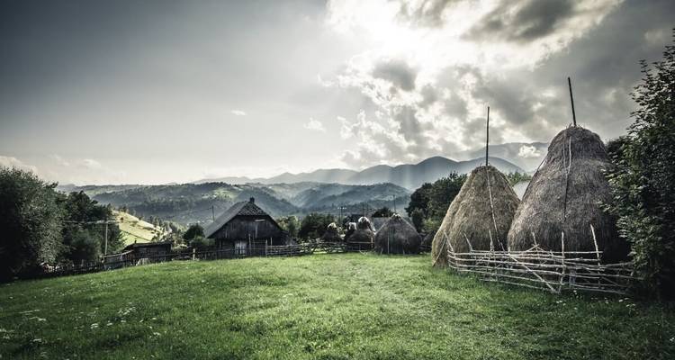 Paysage rural pittoresque avec meule de foin traditionnelle et toile de fond montagneuse sous un ciel dramatique.