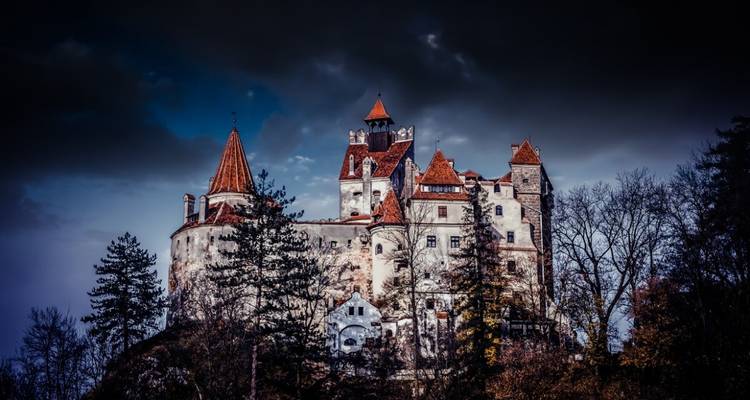 Une vue dramatique d'un château avec des toits rouges contre un ciel sombre et mélancolique.