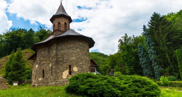 Église en pierre historique entourée d'une végétation luxuriante par une journée ensoleillée.