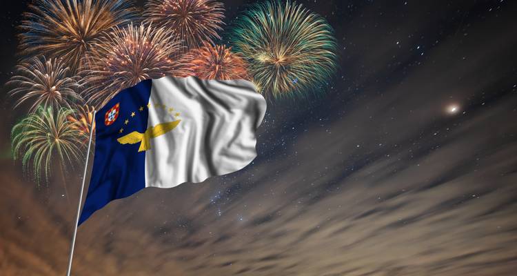 De vlag van de Azoren wappert voor kleurrijk vuurwerk tegen een sterrenhemel.