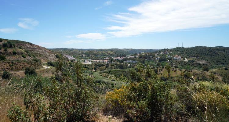 Countryside vista over scattered villages and rolling green hills beneath a blue sky.