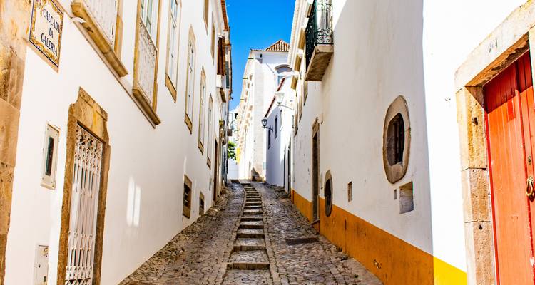 Narrow cobbled lane with whitewashed buildings and bright yellow trim under a vivid blue sky in Faro old town.